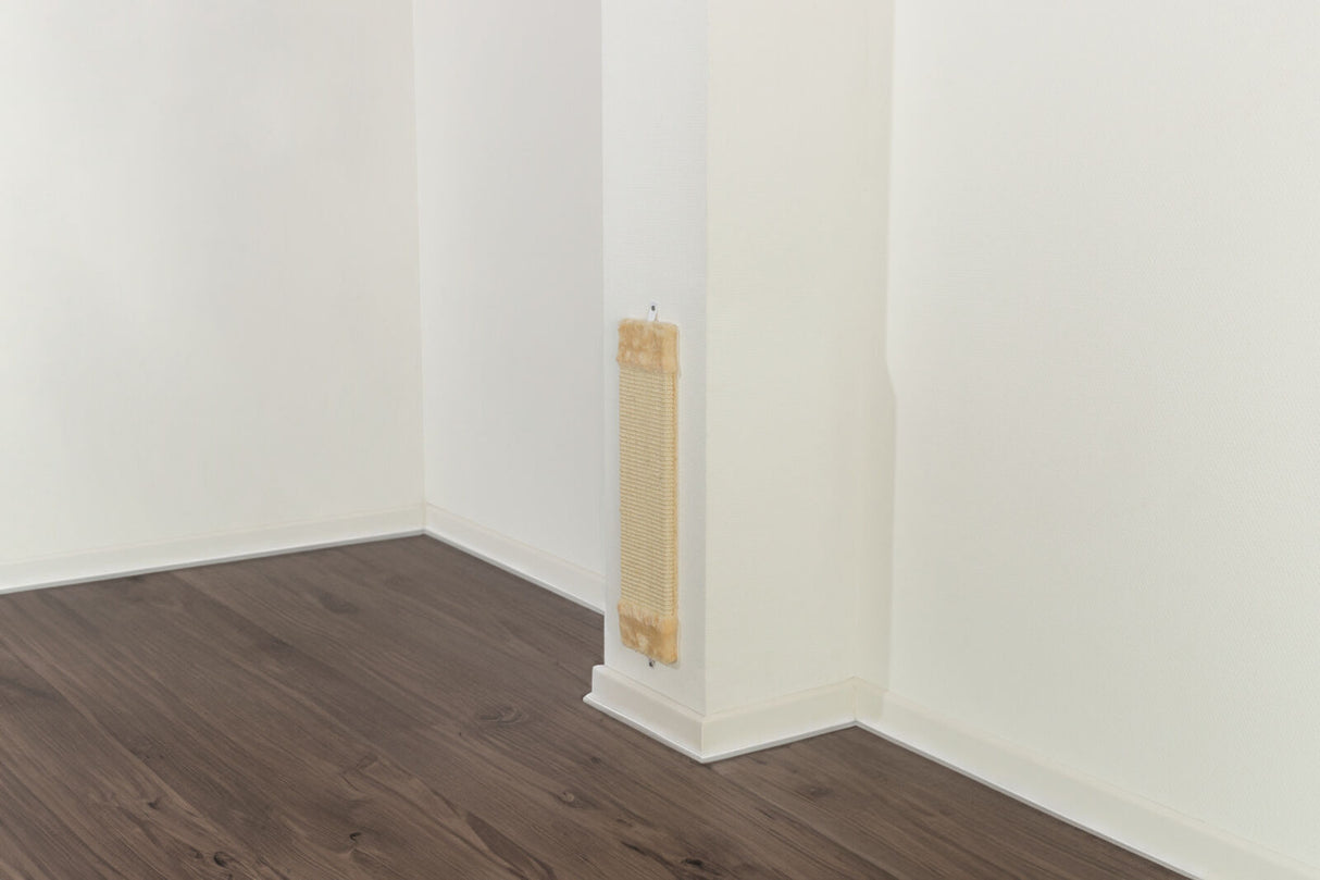 Beiger Kratzbrett an einer weißen Wandecke, darüber hölzerner Boden und weiße Sockelleisten.