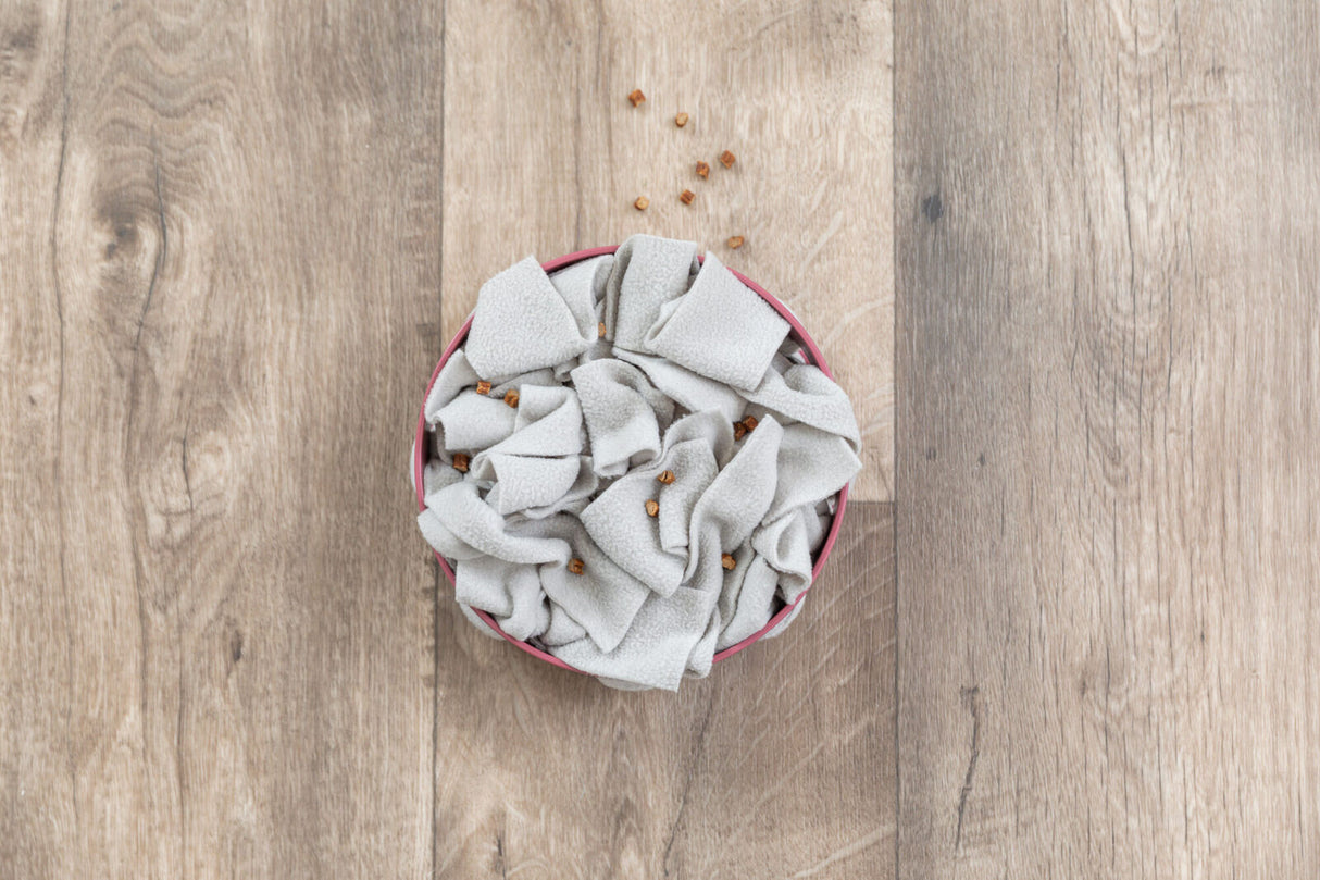 Graue Stofffetzen liegen locker in einer runden Schale auf einem Holzuntergrund, dazwischen sind kleine, braune Stücke verteilt.