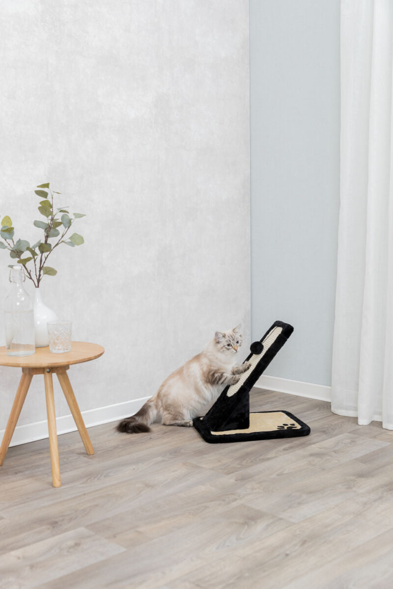 Eine Katze kratzt an einem schwarzen Kratzbrett in einer hellen Ecke mit Holzboden und einem kleinen Tisch.