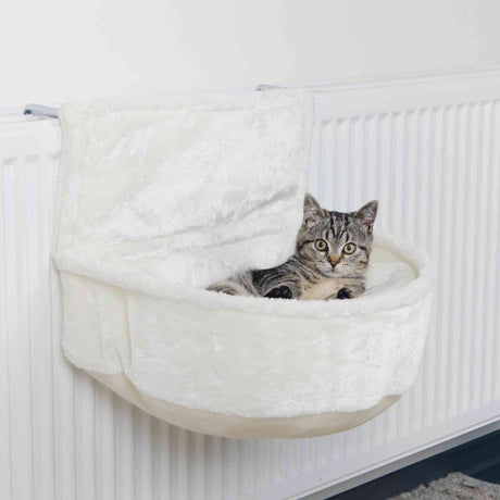 Ein graues Kätzchen liegt in einem weißen, hängenden Katzensitz, der an einem Heizkörper befestigt ist.