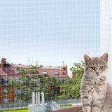 Eine graue Katze sitzt auf einem Balkon vor einem Schutznetz mit Blick auf Bäume und Gebäude im Hintergrund.