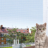 Eine graue Katze sitzt auf einem Balkon vor einem Schutznetz mit Blick auf Bäume und Gebäude im Hintergrund.