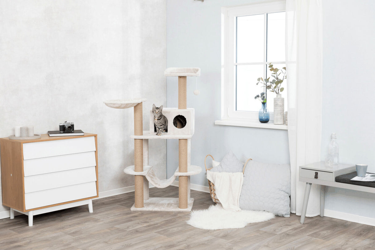 Ein grauer Kratzbaum mit einer Katze darauf steht in einem hell eingerichteten Raum mit Kommode und Fenster.