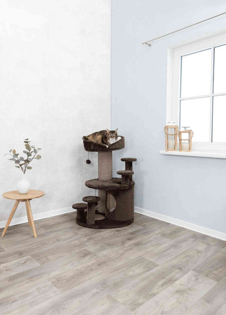 Ein brauner Kratzbaum mit Plattform steht in einer Ecke eines Raumes, darauf liegt eine Katze auf der oberen Ebene.