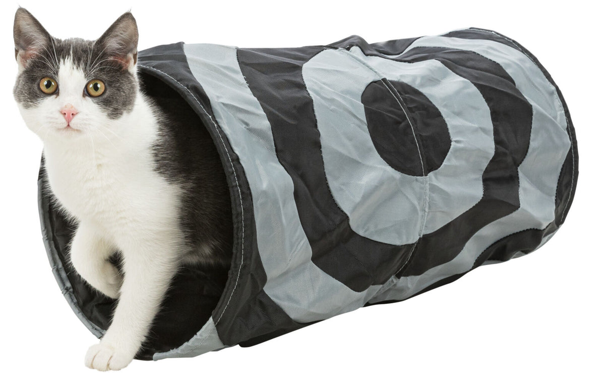Eine schwarz-weiße Katze schaut aus einem schwarz-grauen Tunnel mit kreisförmigem Muster.