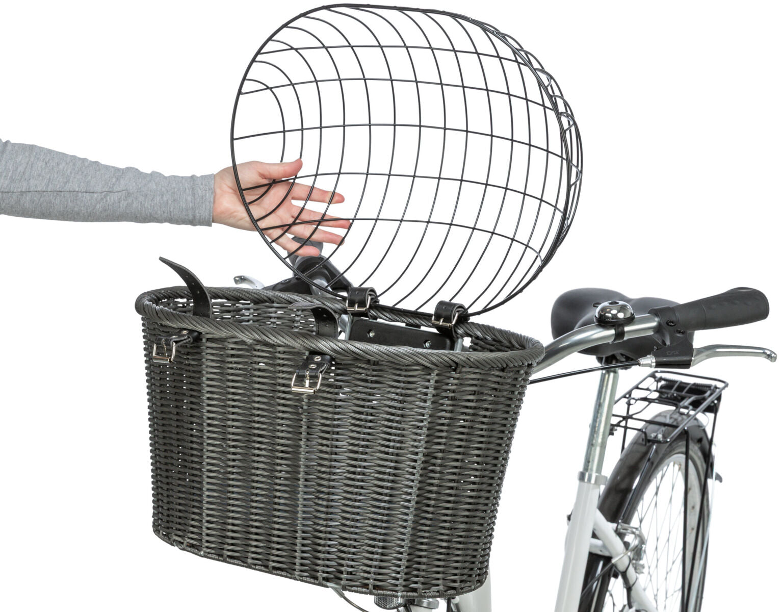 Grau geflochtener Fahrradkorb mit Metallgitterabdeckung auf einem weißen Fahrrad, eine Hand hebt die Abdeckung an.