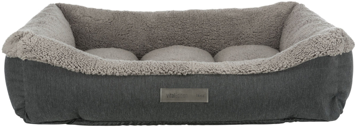 Graues Haustierbett mit weichem, hellgrauem Innenfutter und rechteckiger Form, Label "vital Edition TRIXIE" an der Seite.