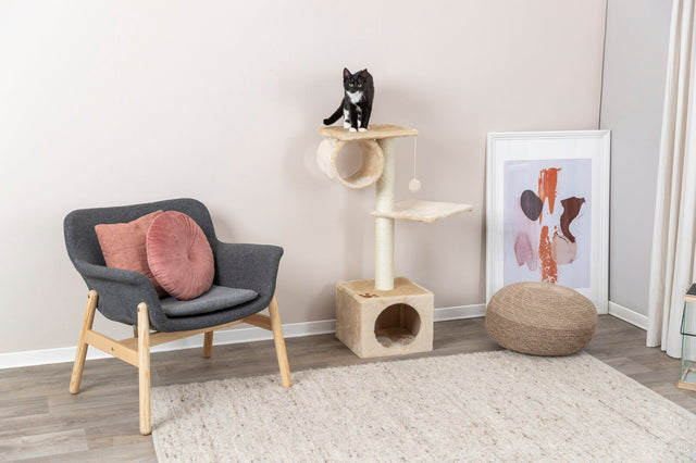 Katzenkratzbaum mit zwei Plattformen, auf dem eine schwarz-weiße Katze sitzt, daneben ein Sessel mit rosa Kissen.