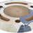 Runde, flache Struktur mit Blättermuster in Blau und Beige, in der Mitte ein kreisförmiges, löchriges Element.