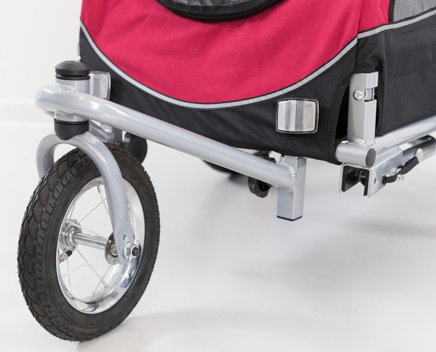 Rotes und schwarzes Fahrradanhänger-Hinterteil mit silbernem Gestell und schwarzem Rad auf weißem Hintergrund.