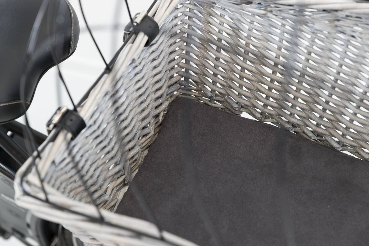 Ein grauer geflochtener Fahrradkorb mit schwarzem Polster, befestigt an einem schwarzen Fahrradsattel.