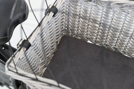 Ein grauer geflochtener Fahrradkorb mit schwarzem Polster, befestigt an einem schwarzen Fahrradsattel.