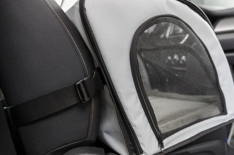 Grau-schwarzes Transportgerät im Auto, mit Netzfenster und Gurt an der Rückenlehne befestigt.