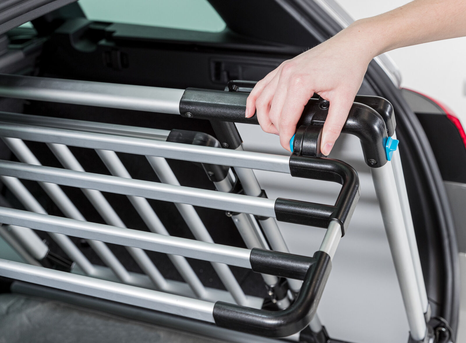Eine Hand justiert ein silbernes Gitter mit schwarzen Elementen im Kofferraum eines Autos.