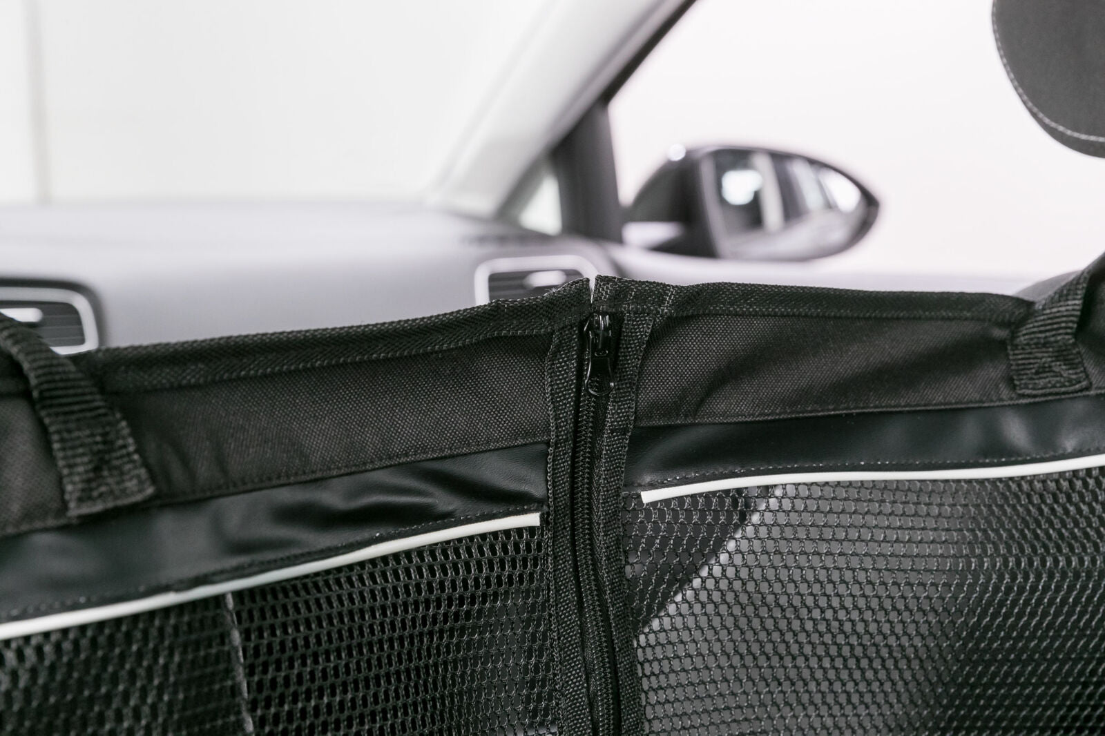 Schwarzes Trennnetz mit Reißverschluss in einem Auto, Hintergrund zeigt verschwommene Autoinnenteile.