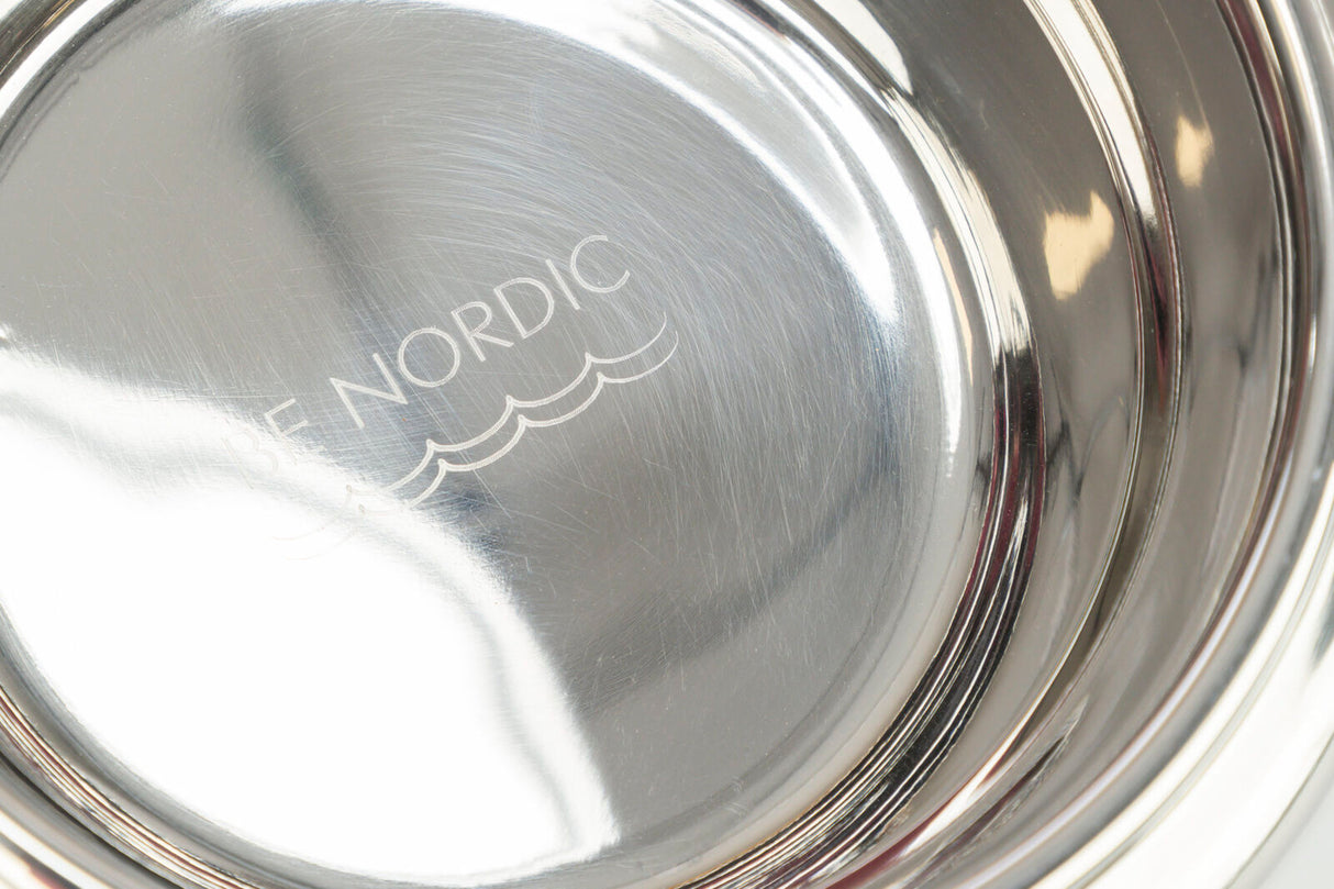 Nahaufnahme einer glänzenden Metallschale mit der Gravur "BE NORDIC" und wellenförmigen Linien.