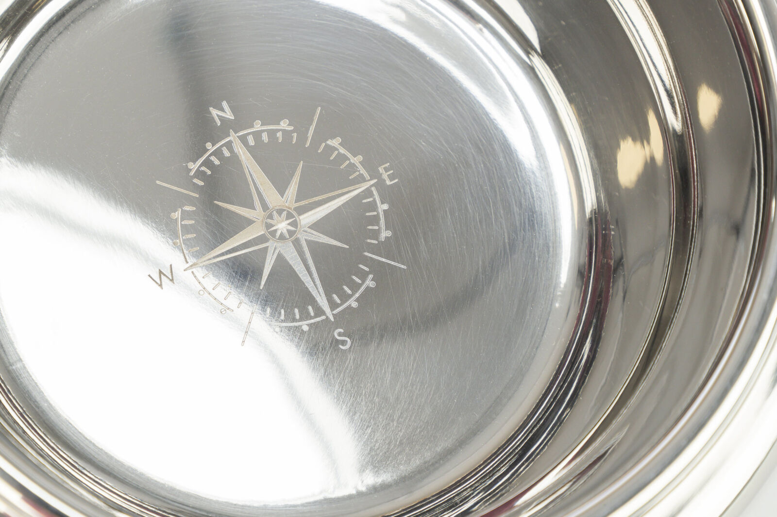 Eine glänzende silberne Metallschale mit einer gravierten Kompassrose im Inneren, die Himmelsrichtungen anzeigt.
