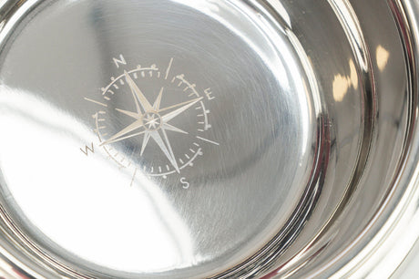 Eine glänzende silberne Metallschale mit einer gravierten Kompassrose im Inneren, die Himmelsrichtungen anzeigt.