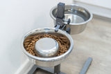 Zwei Edelstahlnäpfe auf einem Ständer, einer mit Trockenfutter, der andere mit Wasser gefüllt.