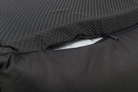 Nahaufnahme eines schwarzen Stoffes mit Punktmuster, ein Reißverschluss ist teilweise geöffnet und darunter ist weißes Material sichtbar.