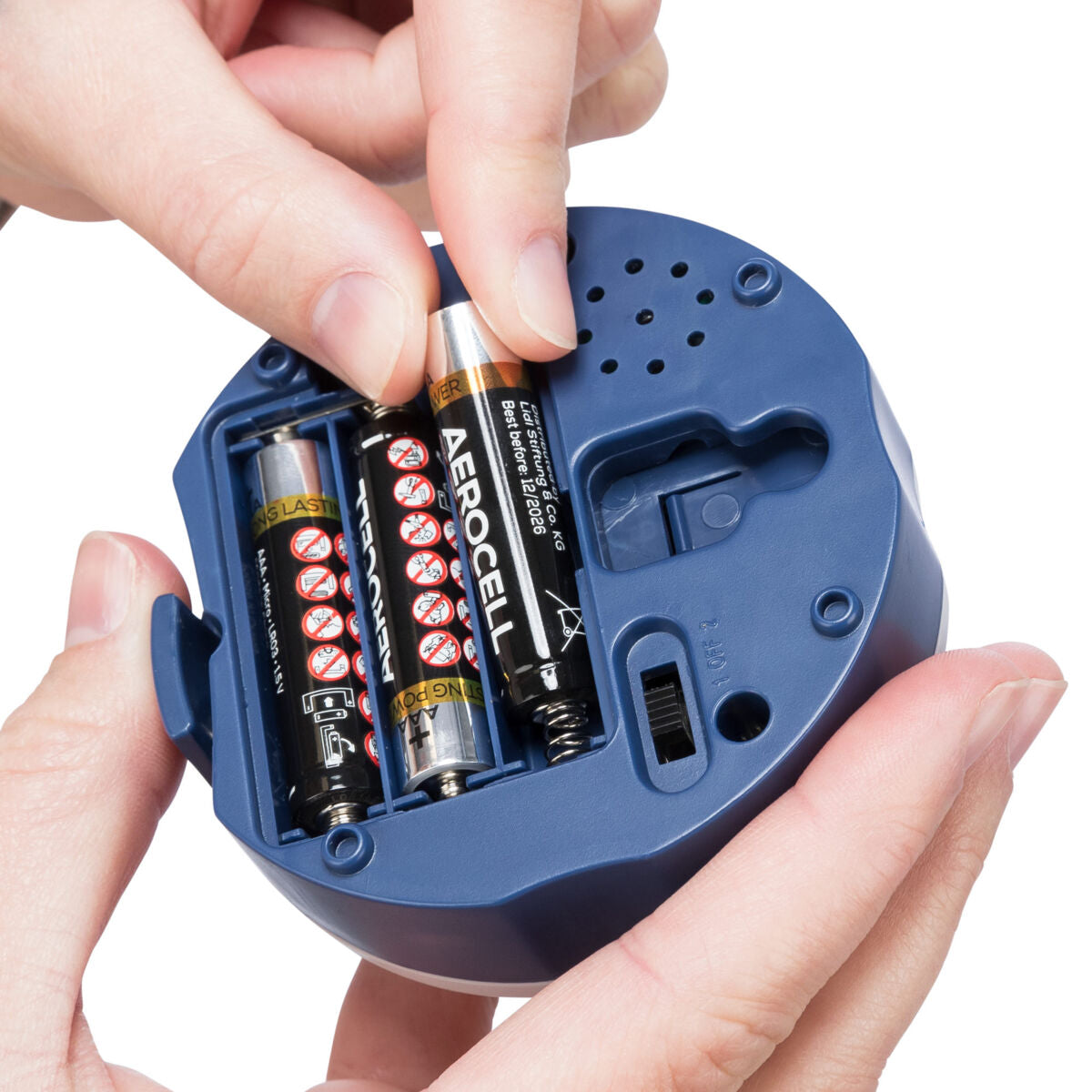 Eine Hand hält ein blaues Gerät mit drei eingelegten Batterien, eine Hand fügt eine Batterie hinzu, sichtbarer Text: "AEROCELL".