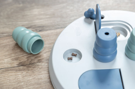 Ein rundes blaugraues Intelligenzspielzeug mit kleinen braunen Hundeknochen auf einer Holzoberfläche.