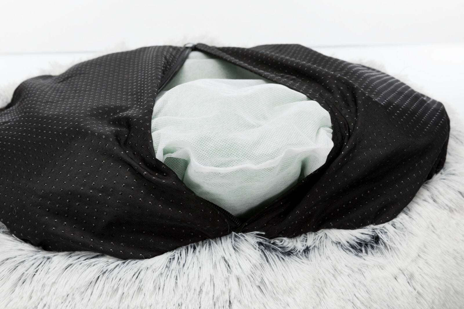 Schwarzer Stoff mit Punkten, darunter weißes Netzmaterial, auf grauem, flauschigem Hintergrund sichtbar.