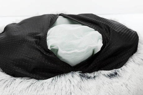 Schwarzer Stoff mit Punkten, darunter weißes Netzmaterial, auf grauem, flauschigem Hintergrund sichtbar.