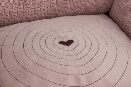 Beiges Kissen mit gestickten konzentrischen Kreisen und einem herzförmigen Muster in der Mitte.