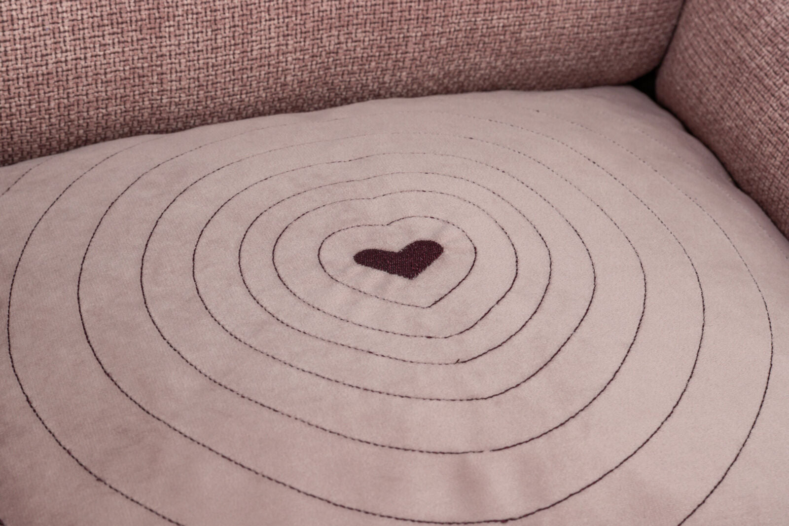 Beiges Kissen mit gestickten konzentrischen Kreisen und einem herzförmigen Muster in der Mitte.