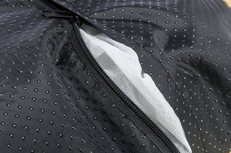 Nahaufnahme eines schwarzen Stoffes mit kleinen Punkten und einem geöffneten Reißverschluss, dahinter weißes Material.