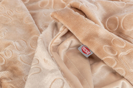 Beige Decke mit aufgestickten runden Mustern und einem roten Etikett mit der Aufschrift "Trixie".