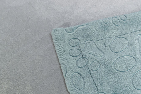 Ecke einer hellblauen, strukturierten Matte mit einem kreisförmigen Muster auf einem grauen Stoffuntergrund.