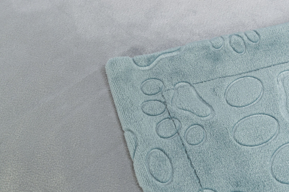 Ecke einer hellblauen, strukturierten Matte mit einem kreisförmigen Muster auf einem grauen Stoffuntergrund.