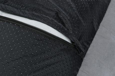 Nahaufnahme eines schwarzen, perforierten Stoffes mit einem sichtbaren Reißverschluss auf grauem Hintergrund.