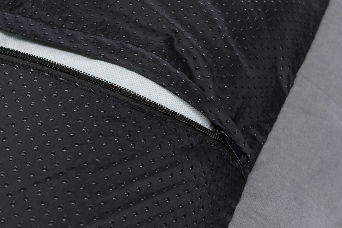 Nahaufnahme eines schwarzen, perforierten Stoffes mit einem sichtbaren Reißverschluss auf grauem Hintergrund.