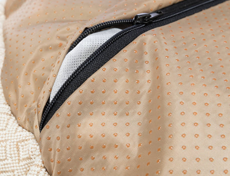Nahaufnahme eines beigefarbenen Textils mit Punktmuster und einem schwarzen Reißverschluss, darunter ein weißes Mesh sichtbar.