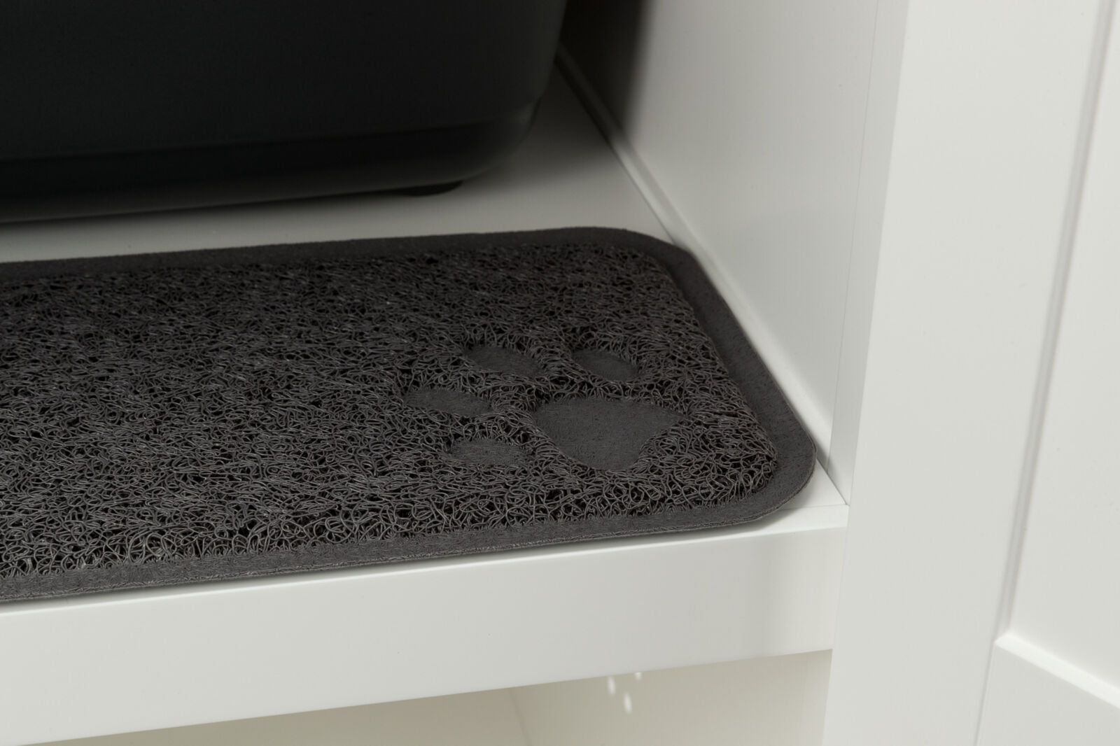 Dunkle Matte mit Pfotenabdruck-Muster auf einem weißen Regal neben einem schwarzen Behälter.