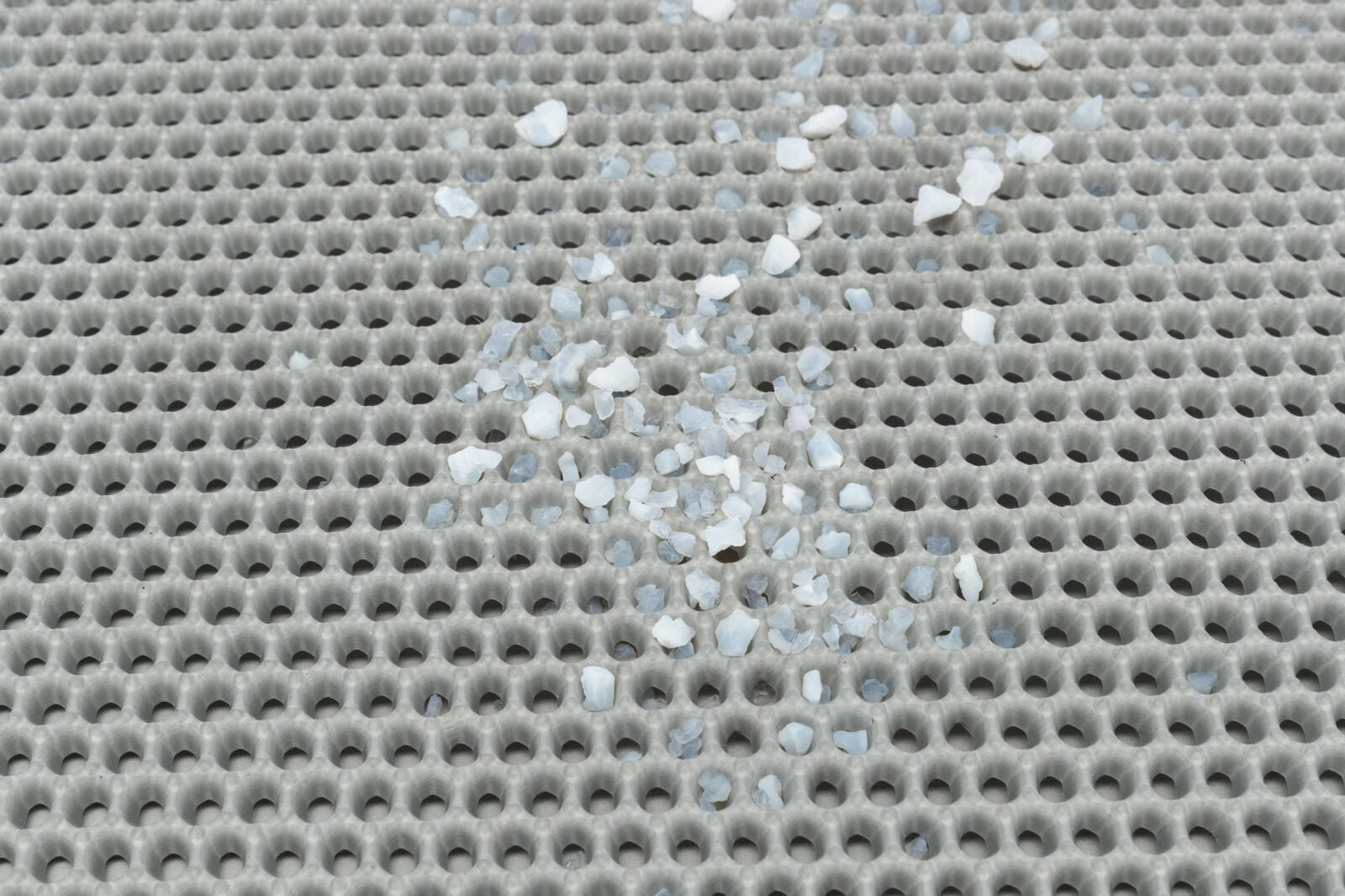 Grau gekreuztes, löchriges Gitter mit verstreuten weißen und blauen Steinchen.