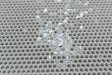Grau gekreuztes, löchriges Gitter mit verstreuten weißen und blauen Steinchen.