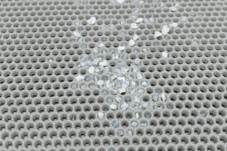 Grau gekreuztes, löchriges Gitter mit verstreuten weißen und blauen Steinchen.