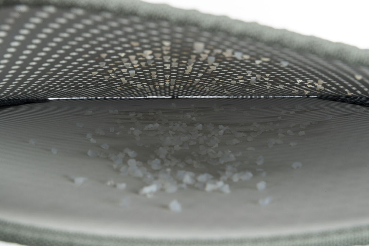 Innenansicht eines grauen, gewölbten Netzes mit kleinen weißen Körnern darauf liegend.