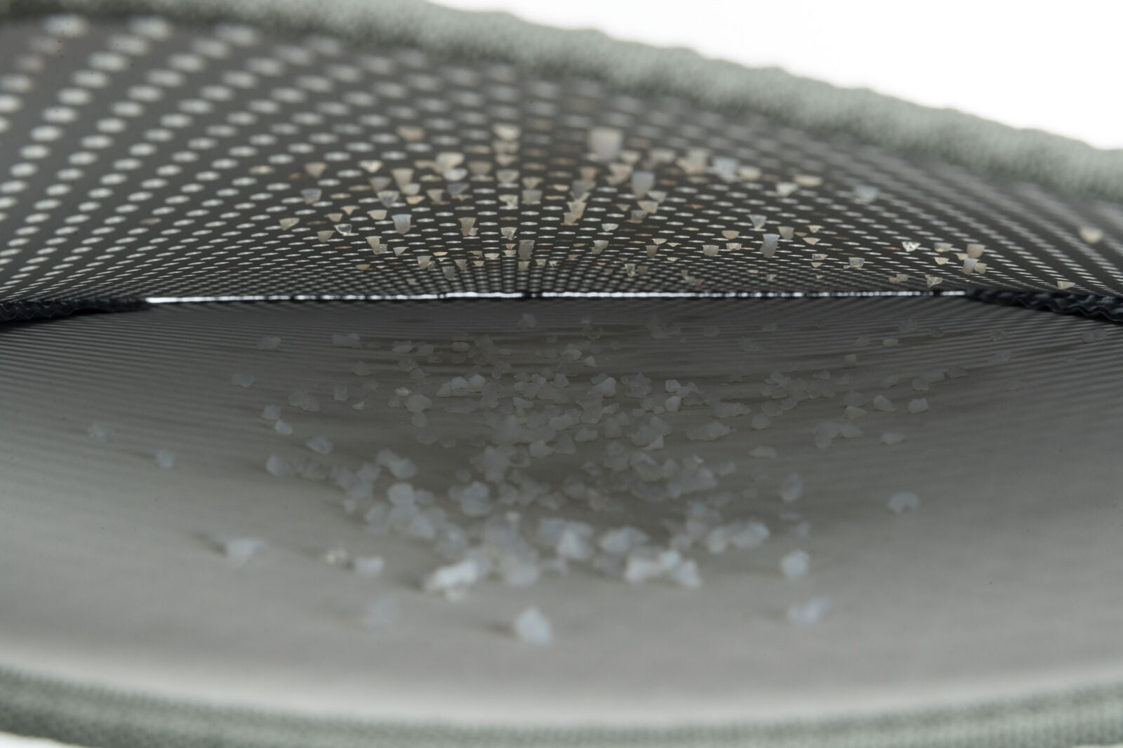 Innenansicht eines grauen, gewölbten Netzes mit kleinen weißen Körnern darauf liegend.