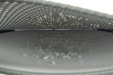 Innenansicht eines grauen, gewölbten Netzes mit kleinen weißen Körnern darauf liegend.