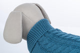 Graues Stofftier mit blauem Strickpullover aus Zopfmuster, weiße Hintergrundfläche.