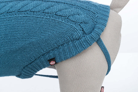 Blauer gestrickter Hundemantel auf beigem stoffbezogenen Modell mit sichtbarem Etikett.