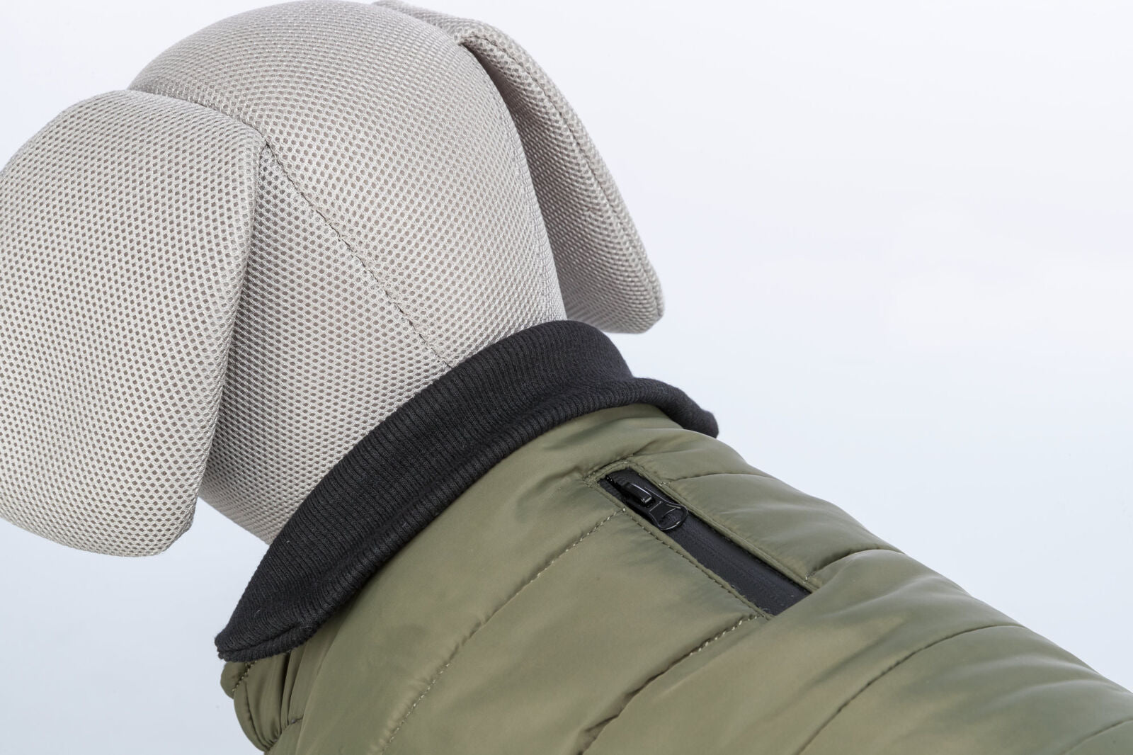 Stofftier in grauer Struktur, trägt eine khakifarbene Hundejacke mit schwarzem Kragen und Reißverschluss.