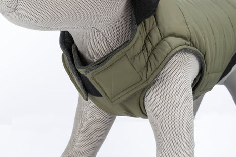 Graues Stoffmodell eines Hundes trägt eine olivgrüne gesteppte Hundejacke mit Klettverschluss.