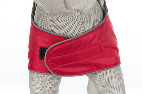 Ein Hundemantel in Rot mit Klettverschluss, getragen von einer Figur aus grauem Netzgewebe.