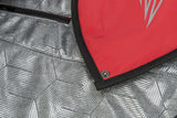 Rotes und silbernes Material mit geometrischem Muster, schwarze Kante und Druckknopf sichtbar.